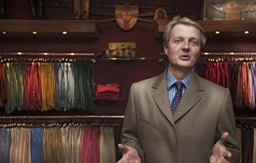 Cordings Managing Director in the Cordings Piccadilly store, wearing a Covert Coat stood in front of a row of corduroy trousers