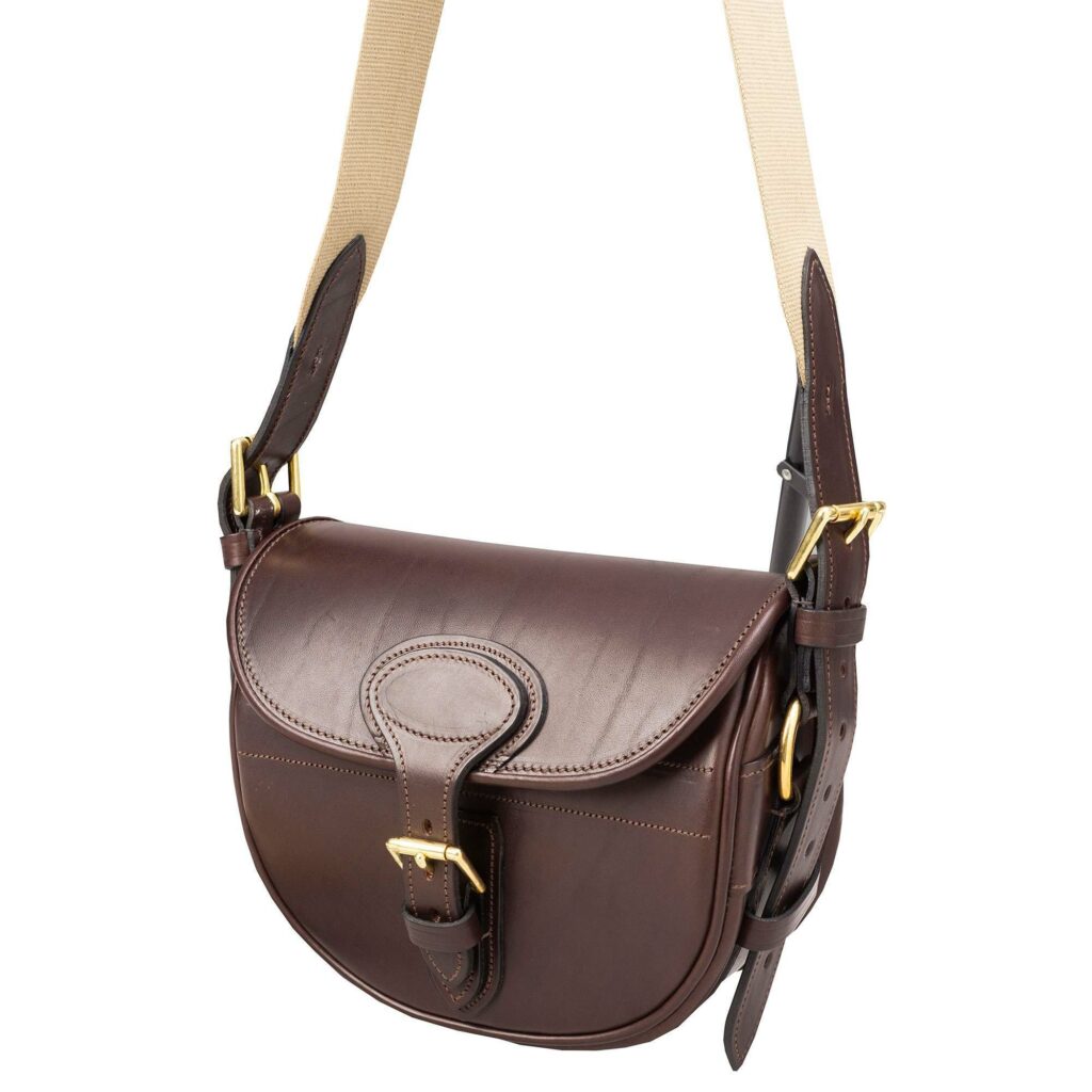  A brown bridle leather cartridge bag with gold buckles and a pale beige handle.