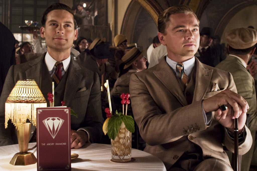 Image of Gatsby and Nick Carraway sat in tan suits, emulating Gatsby style, at a 1920's nightclub from the 2013 film adaptation of The Great Gatsby.