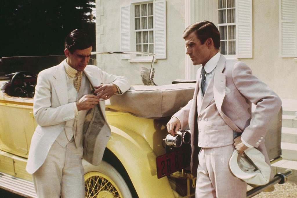 Robert Redford and Sam Waterston stood by a yellow car in true Great Gatsby attire, wearing lightly coloured suits, in the 1974 film adaptation of The Great Gatsby