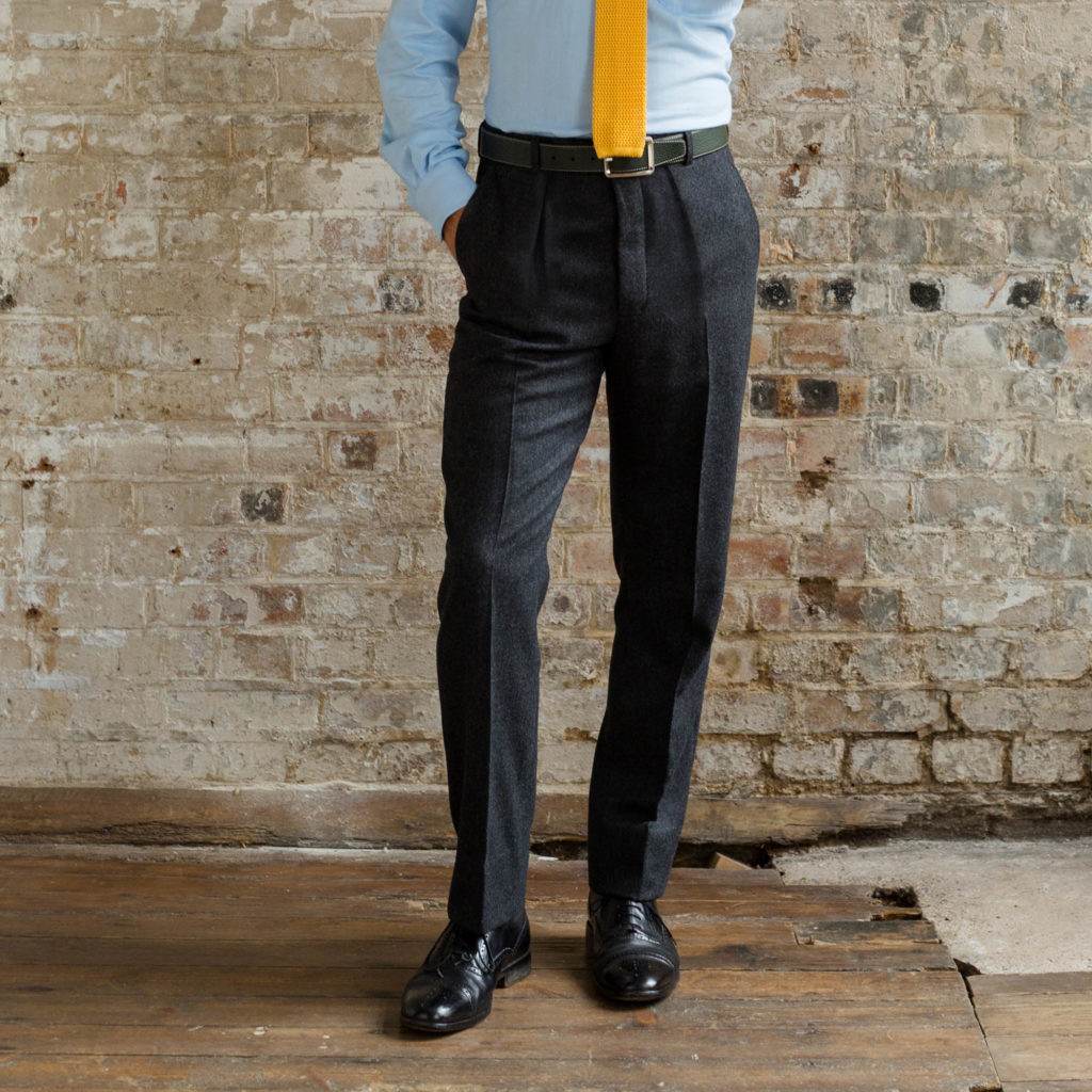 Image of a man wearing classic black flannel trousers, with a blue shirt and a bright yellow knitted tie