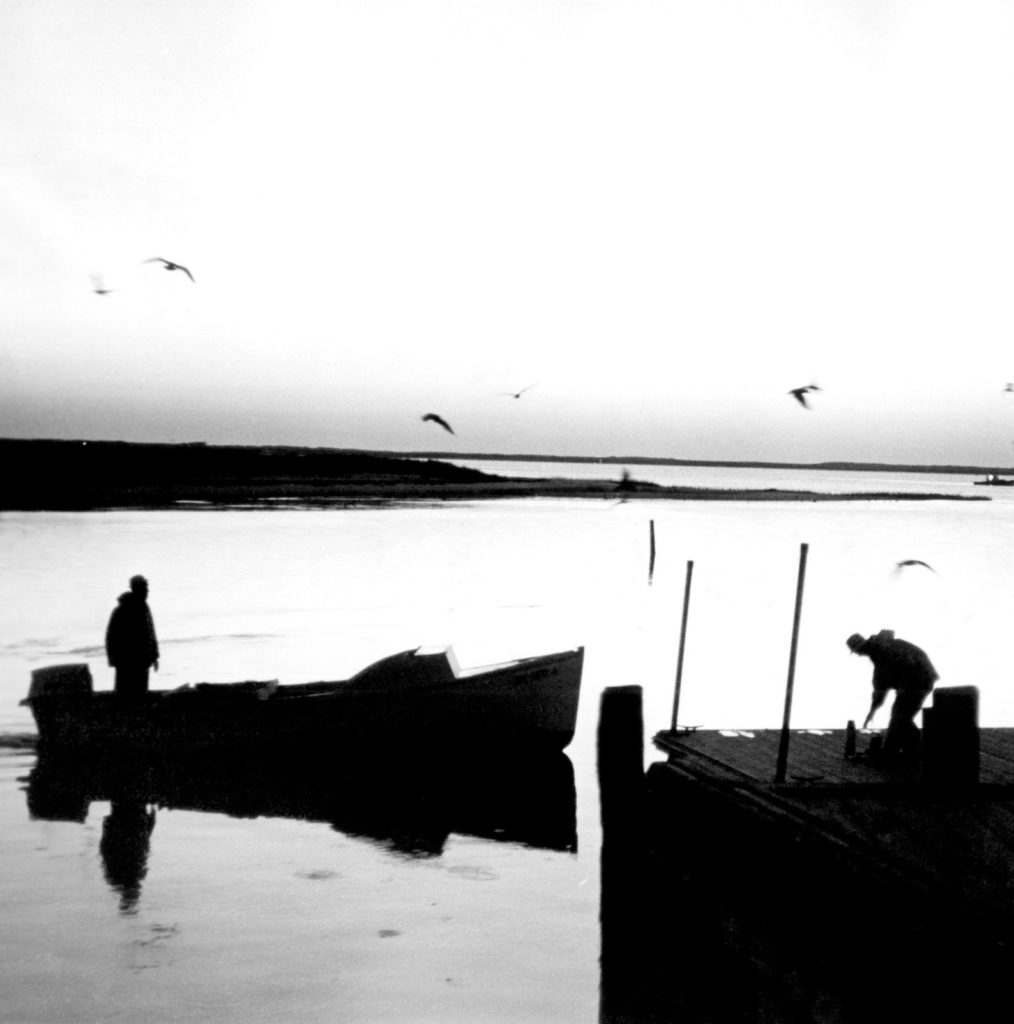 a black and white picture of two people fishing on the coast of New England