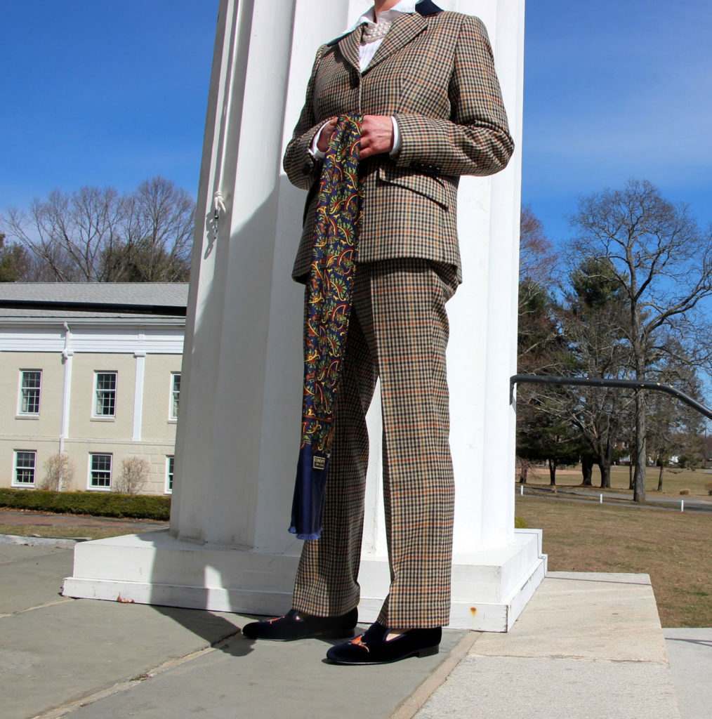 Muffy Aldrich stood by a white pillar in New England USA, wearing a Cordings Wincanton Tweed Suit