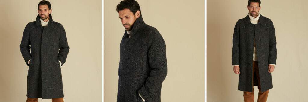 Cordings model in a dark grey raglan sleeve coat. Wearing cinnamon trousers and a white roll neck jumper.